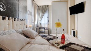 Habitación de hotel con cama, televisión montada en la pared, mesa de comedor y ventana con cortinas.