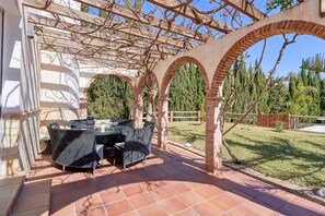 A covered outdoor patio with a table and chairs, brick arches, and a pergola with vines. - Villa 'Casa Alba' with Sea and Mountain View, Pool, Garden & Wi-Fi (Salobreña)