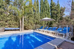 Una piscina con azulejos azules, rodeada de sillas de descanso y una palmera.