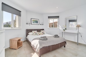 Un dormitorio con cama, mesitas de noche, un escritorio y una ventana.