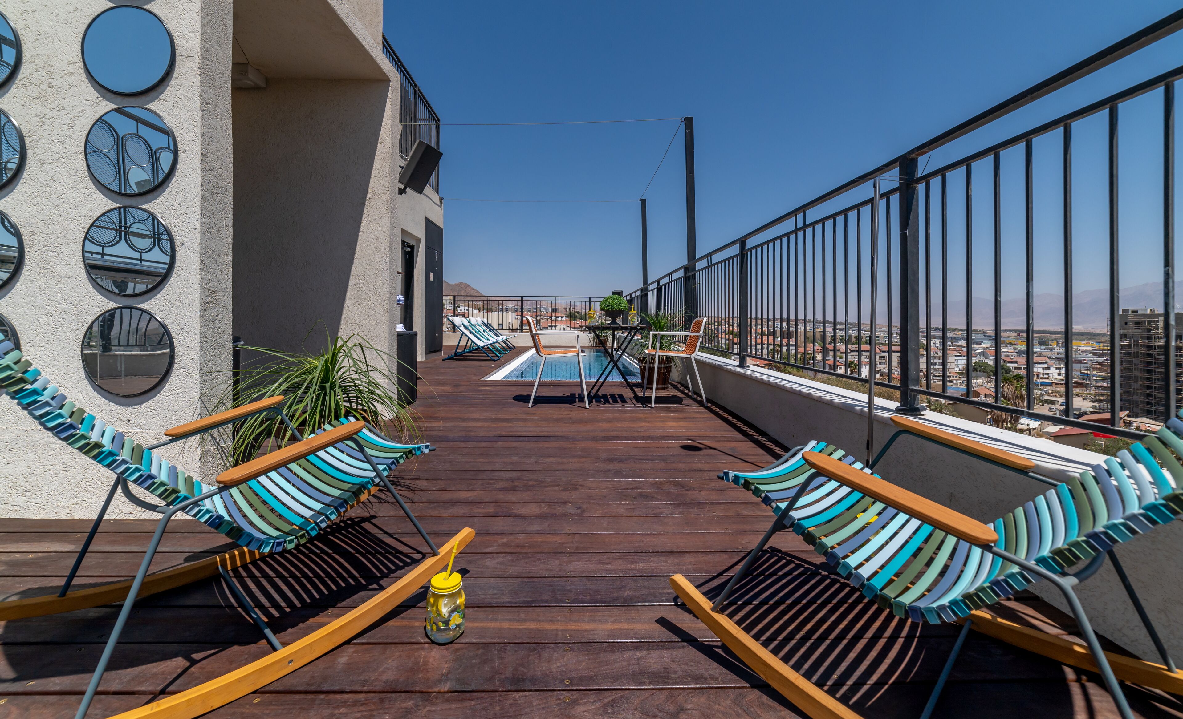 Una terraza en la azotea con piscina, sillas de descanso y vistas de la ciudad.