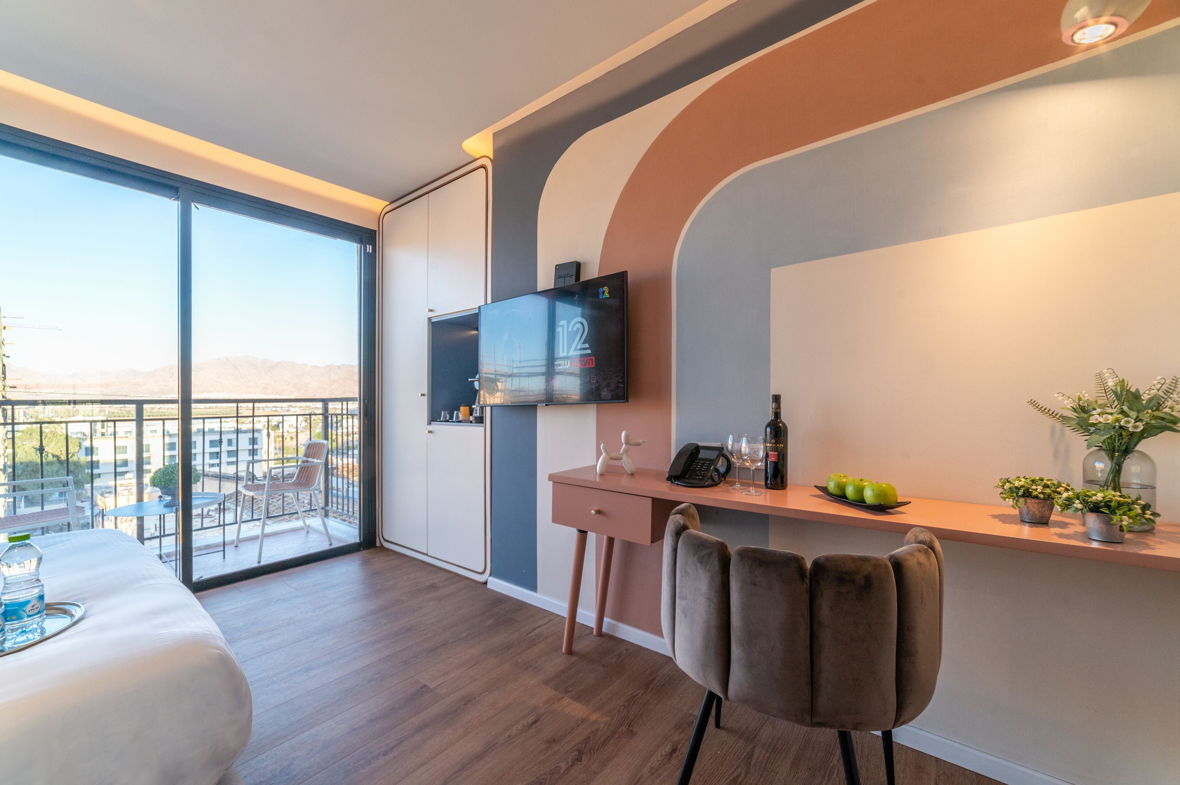 Una habitación de hotel moderna con balcón, un escritorio con silla, una cama y un televisor instalado en la pared.