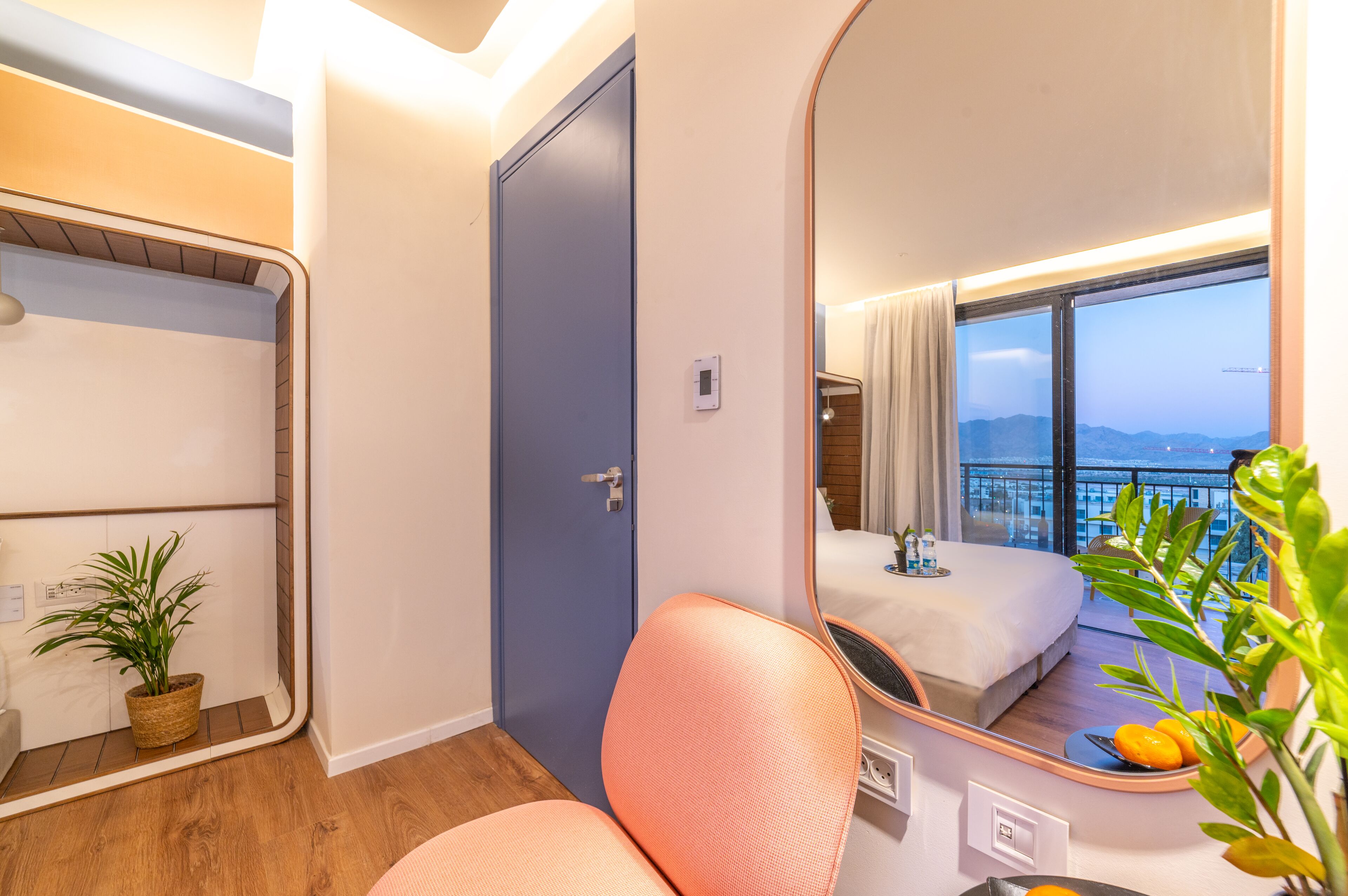 A hotel room with a large mirror reflecting a balcony with a view of the city.