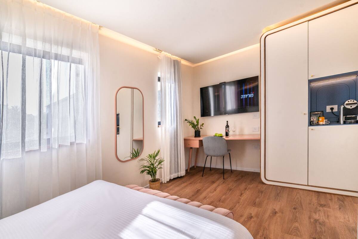A modern hotel room with a bed, a desk, a TV, and a wardrobe.