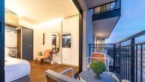 Habitación de hotel moderna con balcón, cama, silla y mesa con planta.