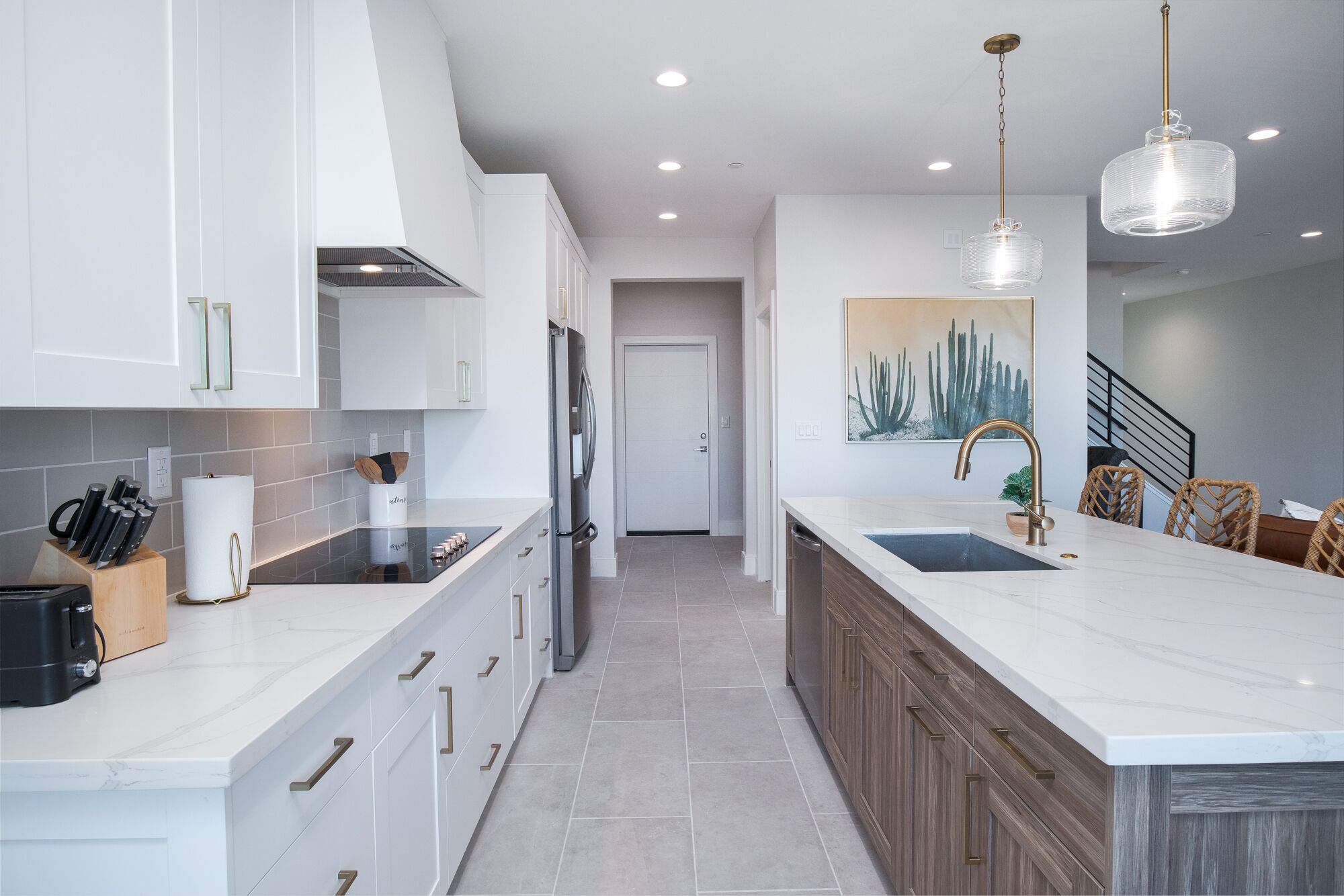 A modern kitchen with white cabinets, a central island with a sink, and a dining area with wicker chairs.