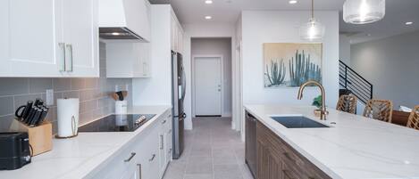 A modern kitchen with white cabinets, a central island with a sink, and a dining area with wicker chairs.