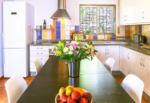 Una cocina moderna con una isla central, armarios blancos, extractor de acero inoxidable y una ventana con barandales decorativos.