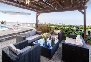 Une terrasse extérieure avec des meubles en osier, une table en verre et une piscine en arrière-plan.