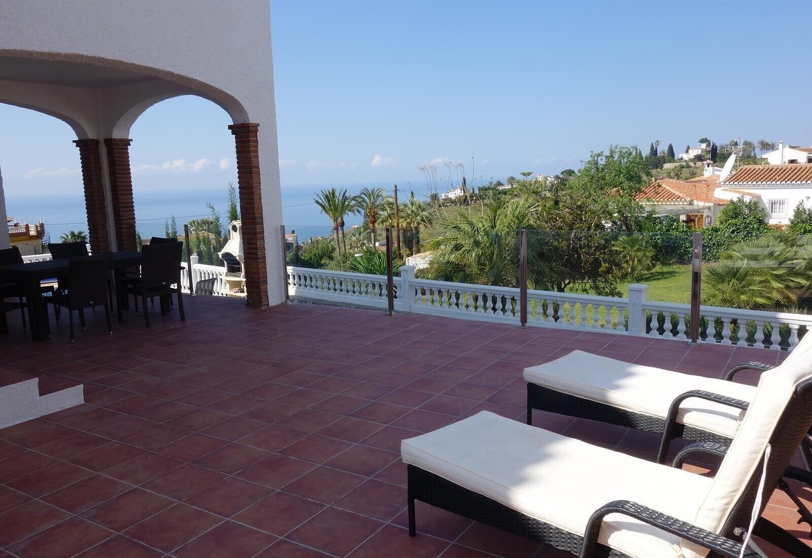 A terrace with a view of the sea, outdoor furniture, and a white railing.