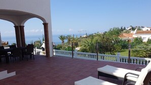 Eine Terrasse mit Meerblick, Gartenmöbeln und einem weißen Geländer.