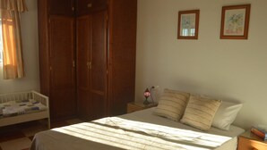 Ein Schlafzimmer mit einem Bett, einem Babybett, einem Kleiderschrank und zwei gerahmten Bildern an der Wand.