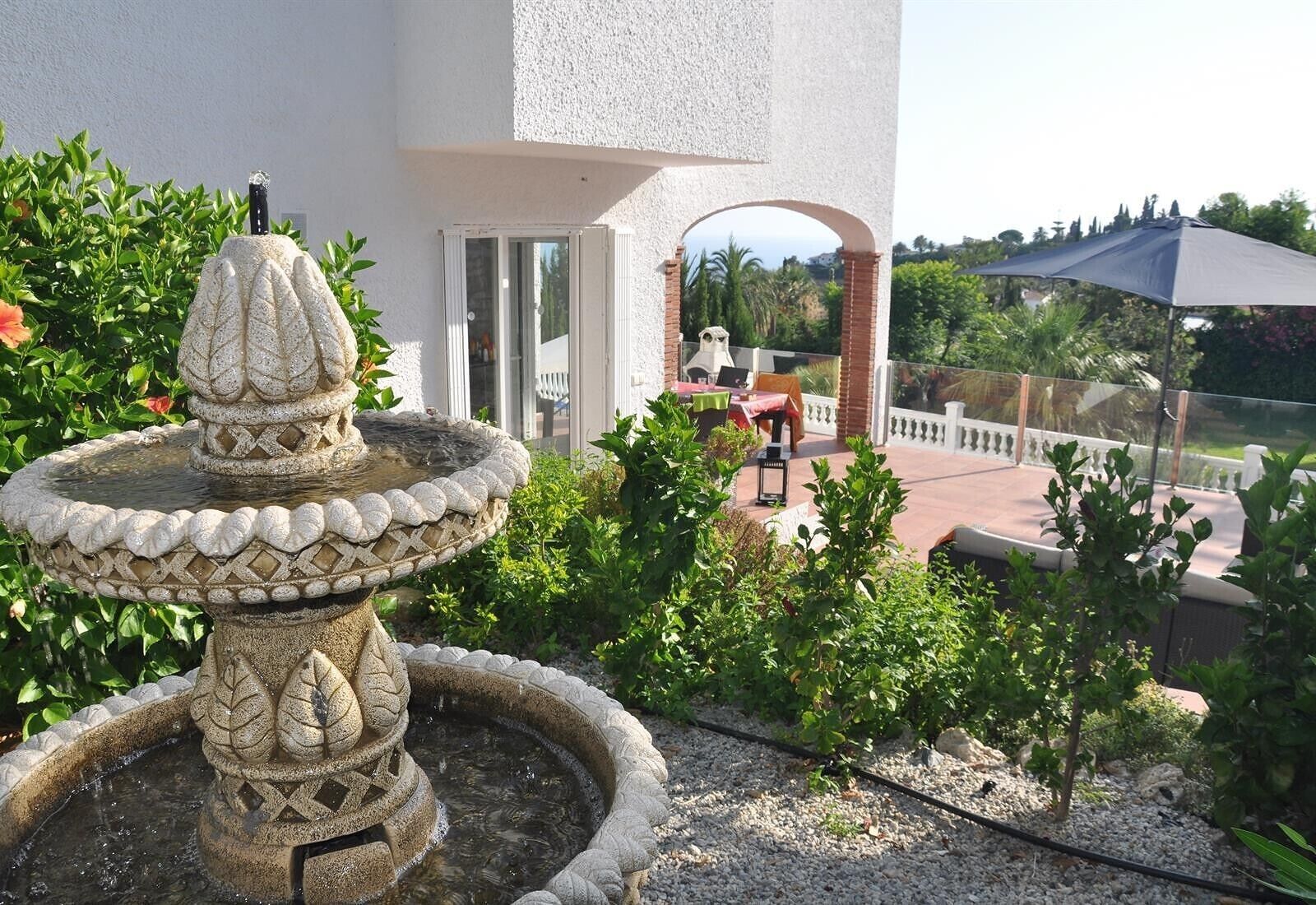 A stone fountain, a patio with a table and chairs, and a covered seating area.