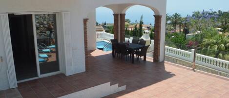 Une terrasse couverte avec une piscine, des sièges d’extérieur et une vue sur la mer.