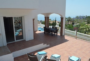 Une terrasse couverte avec une piscine, des sièges d’extérieur et une vue sur la mer.
