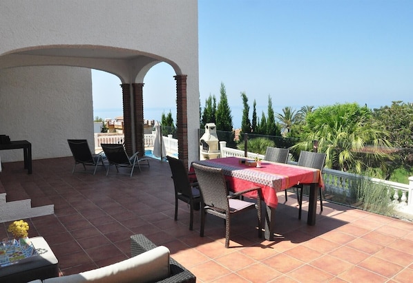 Une terrasse avec une table et des chaises, une piscine et une vue sur la mer.