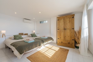 Un dormitorio con dos camas, un armario de madera, un ventanal pequeño y una lámpara de pie.