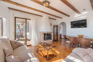Una sala de estar con sofá, una mesa de centro de vidrio, chimenea y un comedor con sillas y una mesa.