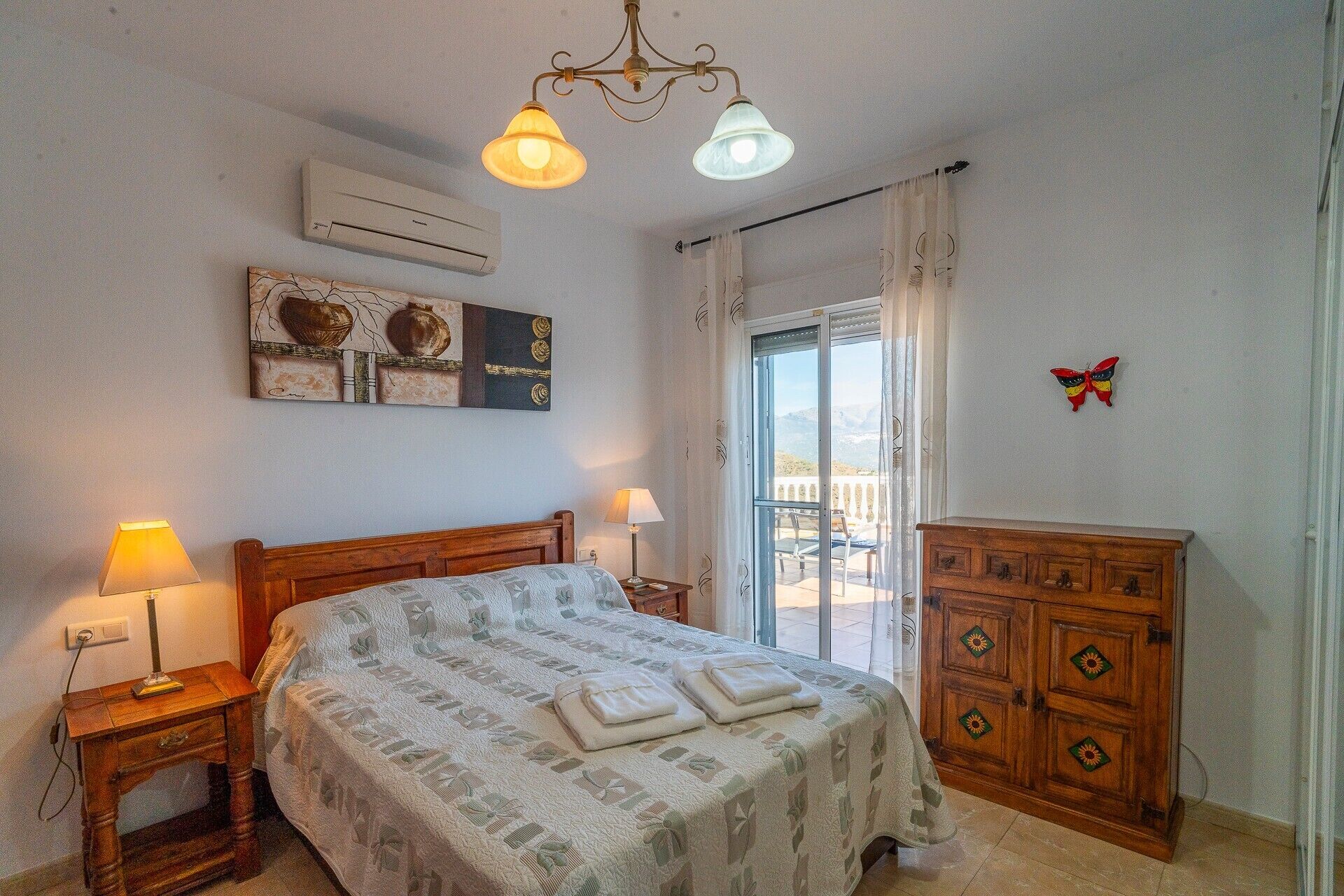 A bedroom with a bed, bedside lamps, an air conditioner, a dresser, and a butterfly decoration.