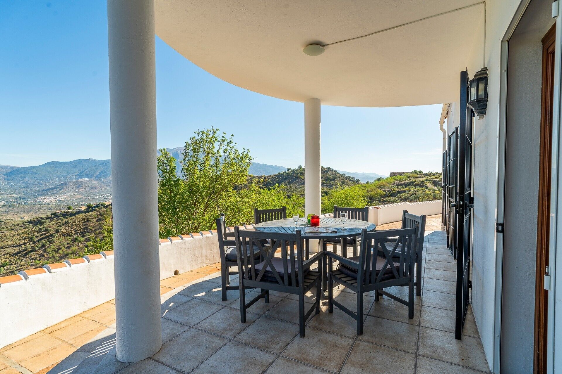 A terrace with a table and chairs, a view of the countryside, and a building with a door.