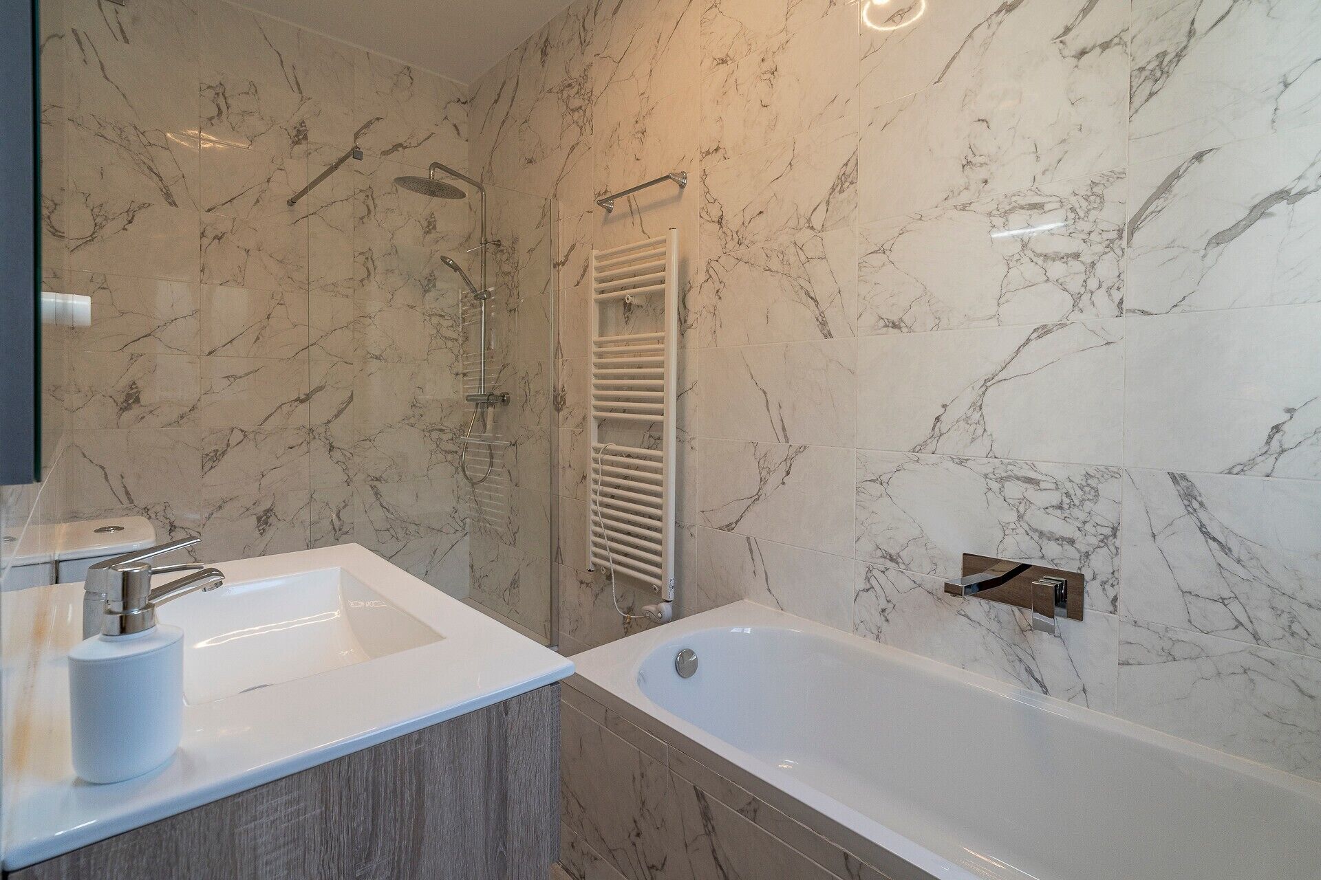 A bathroom with a marble wall, a sink, a bathtub, and a shower.