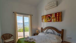 Quarto com cama, poltrona, quadro e ar condicionado.