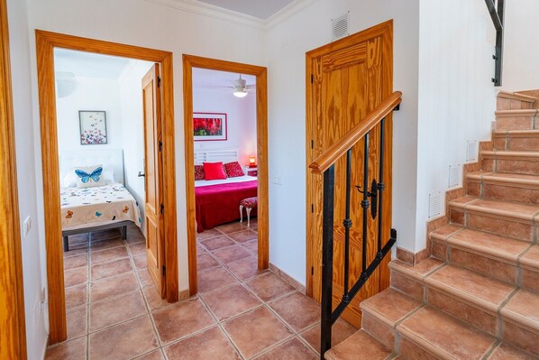 Un couloir mène à une chambre où se trouvent un lit, une couverture rouge et un tableau accroché au mur.