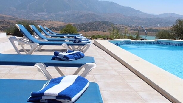 A poolside area with lounge chairs and a swimming pool, surrounded by mountains. - Villa Las Alondras with Lake and Mountain View, Pool, Garden & Wi-Fi (La Viñuela)
