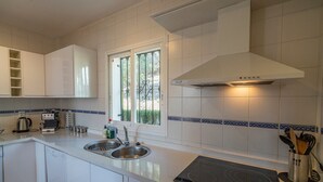 A modern kitchen with white cabinets, a double sink, a coffee maker, and a window with a view. - Villa Maroma with Mountain View, Pool, Garden & Wi-Fi (La Viñuela)