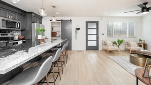 A modern kitchen with a marble countertop, bar stools, and pendant lighting.