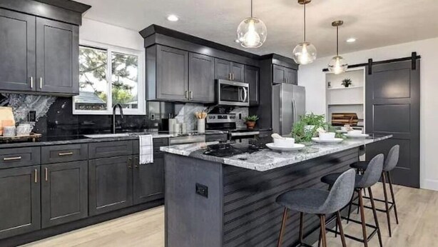 A modern kitchen with dark cabinetry, a central island with bar stools, a microwave, and a sink.
