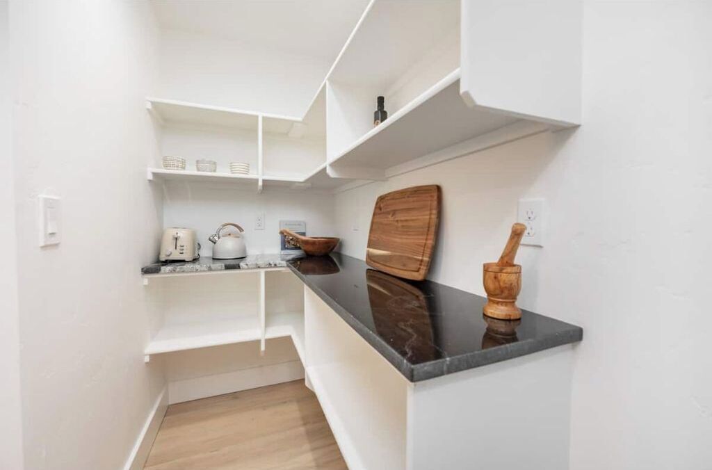 A compact kitchen with white cabinetry, a black countertop, and a wooden cutting board.