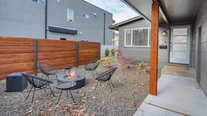 An outdoor patio with a fire pit and seating, a wooden fence, and a building with a gray exterior.