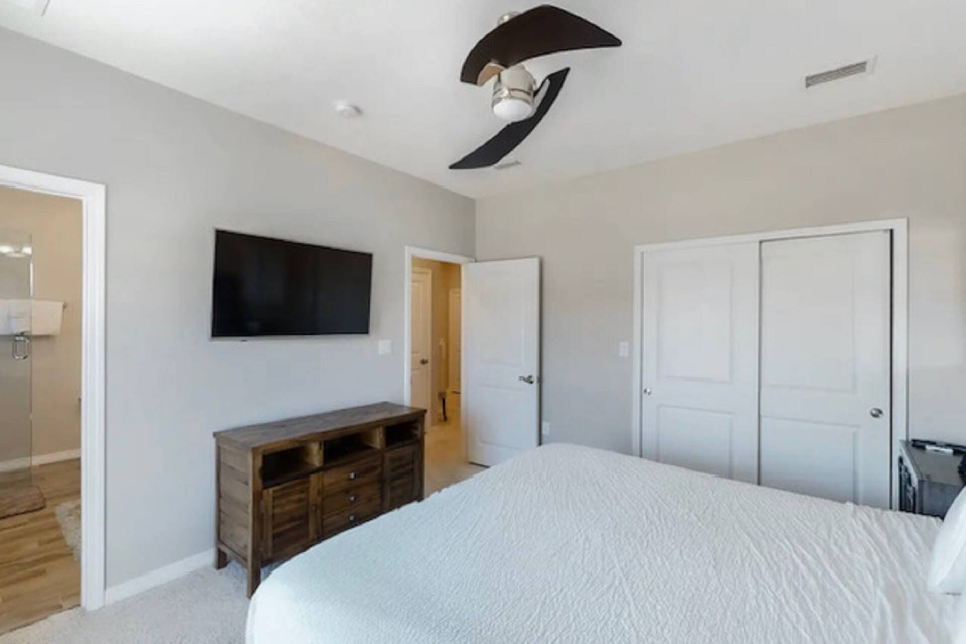 A bedroom with a bed, a television, a wardrobe, and a ceiling fan.