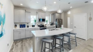 Una cocina moderna con una isla grande, electrodomésticos de acero inoxidable e iluminación colgante.