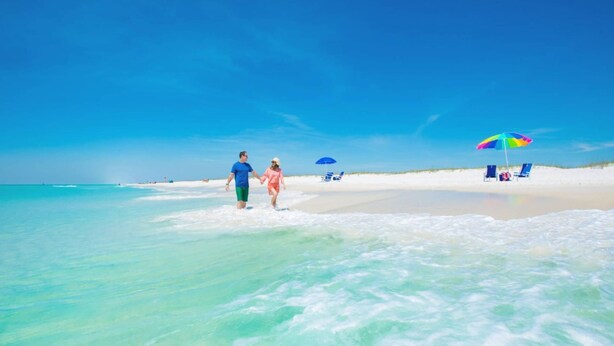 Una playa con agua turquesa cristalina, una orilla arenosa y algunas sombrillas.