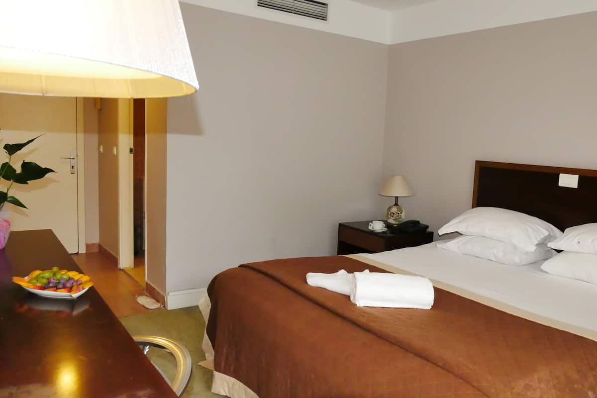 A hotel room with a neatly made bed, a bedside table with a lamp, a small table with fruit, and a potted plant.