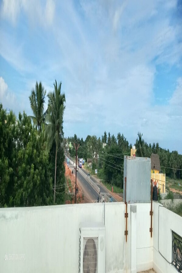 A view from a balcony overlooking a road with palm trees and buildings in the distance. - Rainbow Residency ECR (Vanur)