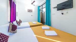 A hotel room with two beds, a flat-screen TV mounted on the wall, a ceiling fan, and a window with curtains. - Rainbow Residency ECR (Vanur)
