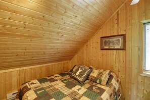 A bedroom with a sloped ceiling, wooden walls, a bed with a patterned quilt, and a framed picture on the wall. - Cabin w/ Fireplace < 1 Mile to Lakes + Golf (Pequot Lakes)