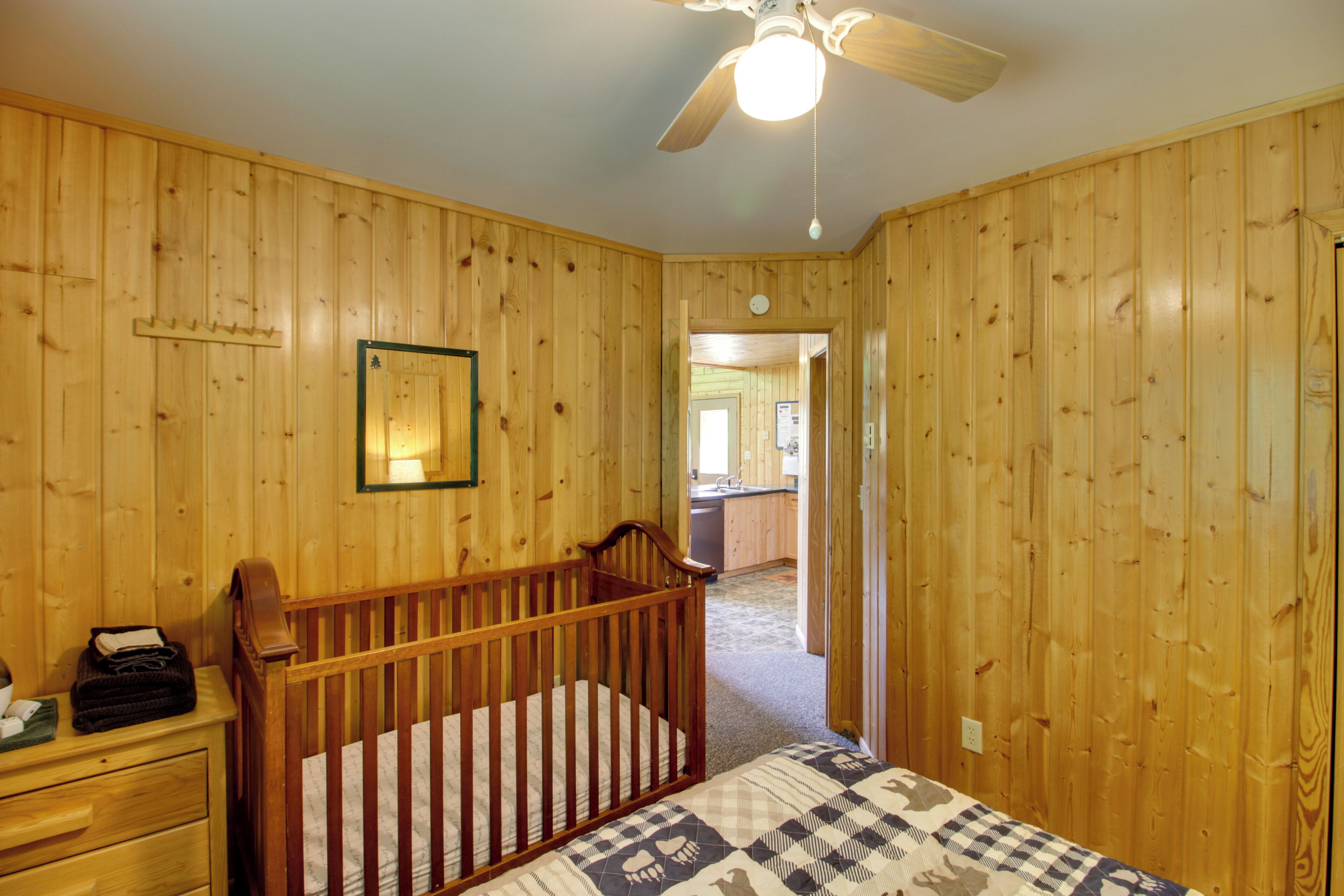 Una habitación con paneles de madera, una cuna, un aparador y un ventilador de techo.