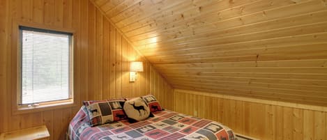 A bedroom with a wooden ceiling, a bed with a patterned quilt, a nightstand, a window with blinds, and a ceiling fan.