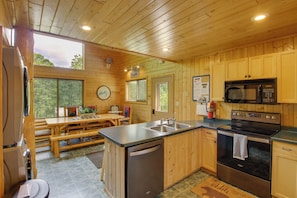 Interior de una cabaña de madera con cocina, comedor y vistas al exterior.