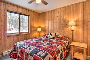 Une chambre avec un mur lambrissé en bois, une grande fenêtre, une couvre-lit matelassé, deux lampes de chevet et une table de chevet en bois.