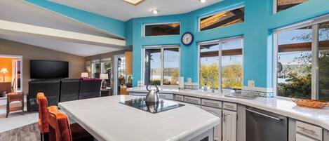 A modern kitchen with a central island, large windows, and a view of the outdoors.