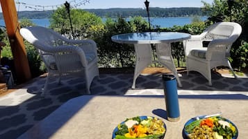 En patio med to fletstole og et rundt bord, med udsigt over en sø med skovkant.