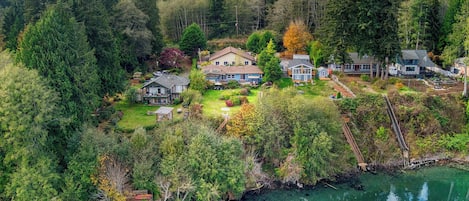 A residential area with houses surrounded by dense forest and a body of water.