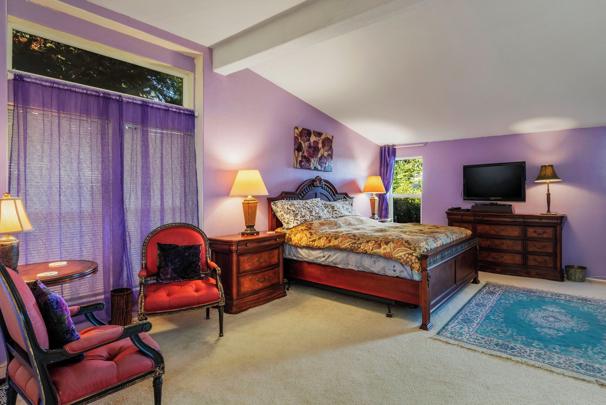 A bedroom with a bed, two nightstands, a chair, a TV, and a window with curtains.