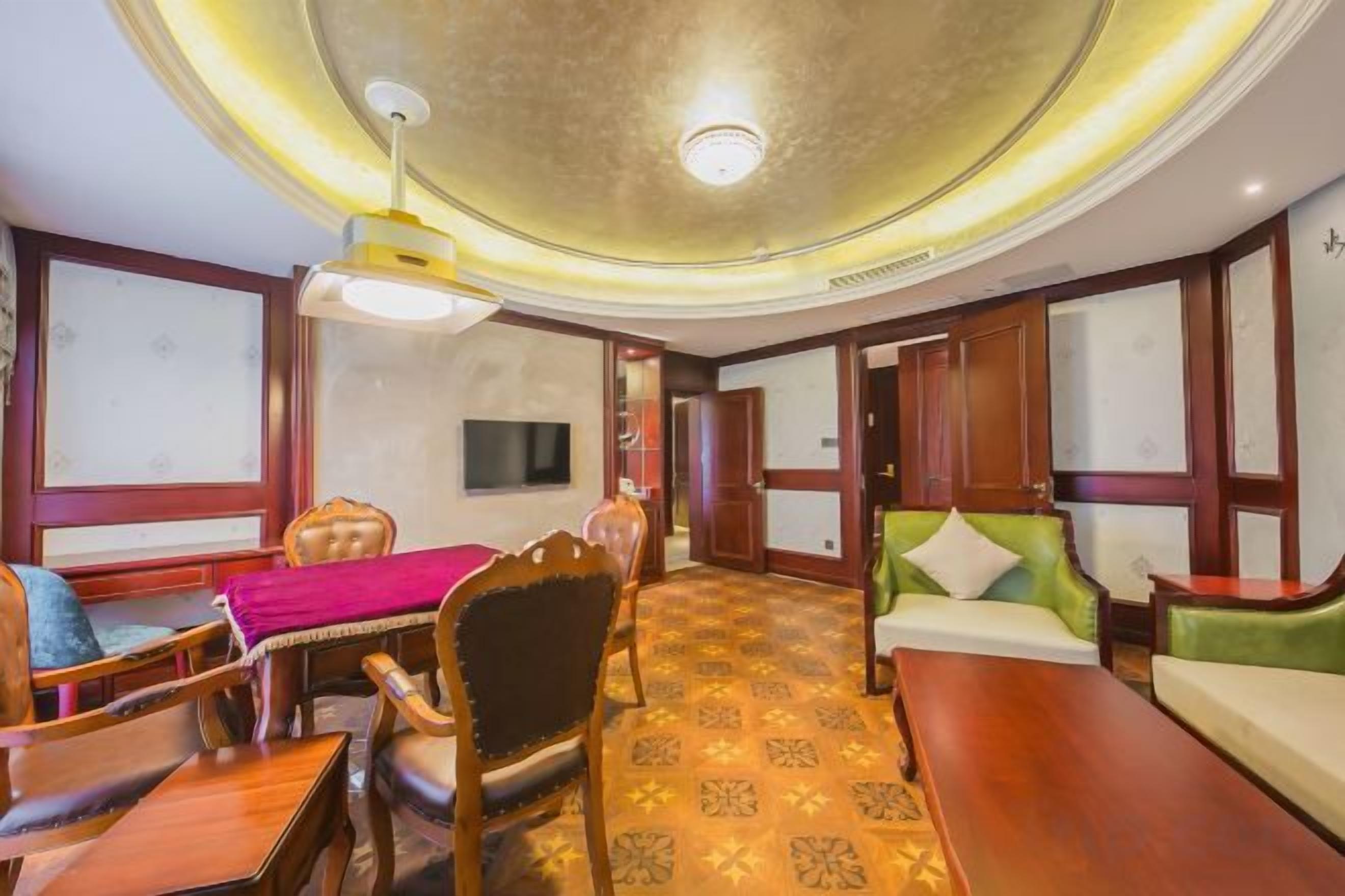 A hotel room with a dining area, a sofa set, a television, and a patterned carpet.