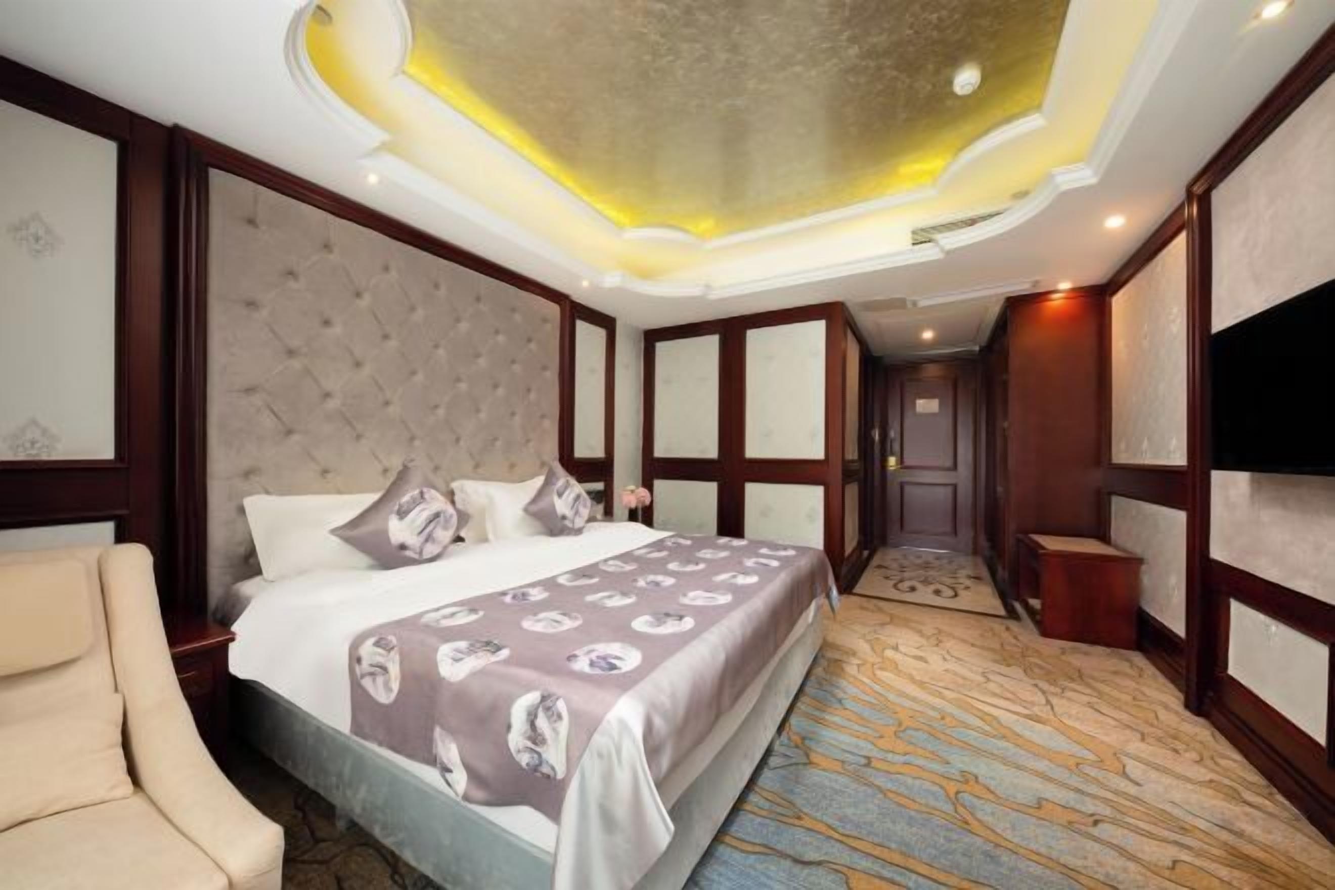 A hotel room with a large bed, a sofa, a television, and a carpeted floor.